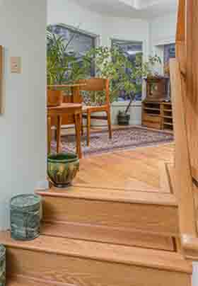 Teak desk, chair at top of oak stairs with plants on window side of room with beige, burgundy Oriental carpet