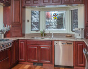 Kitchen with stainless steel appliances and cherry cabinets on all sides, bay windows, marble counters, wood floor.