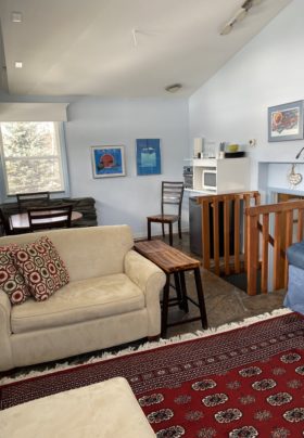 Light blue room with day bed, sofa, table with four stools, red patterned Oriental carpets; free-standing soap stone fireplace