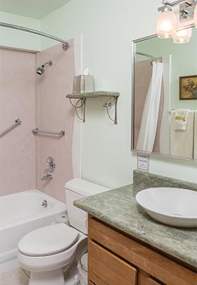 Green granite counter with white vessel sink, white toilet and tub with showerhead