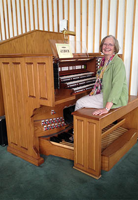 Caroline in green jacket with floral scarf seated on organ bench