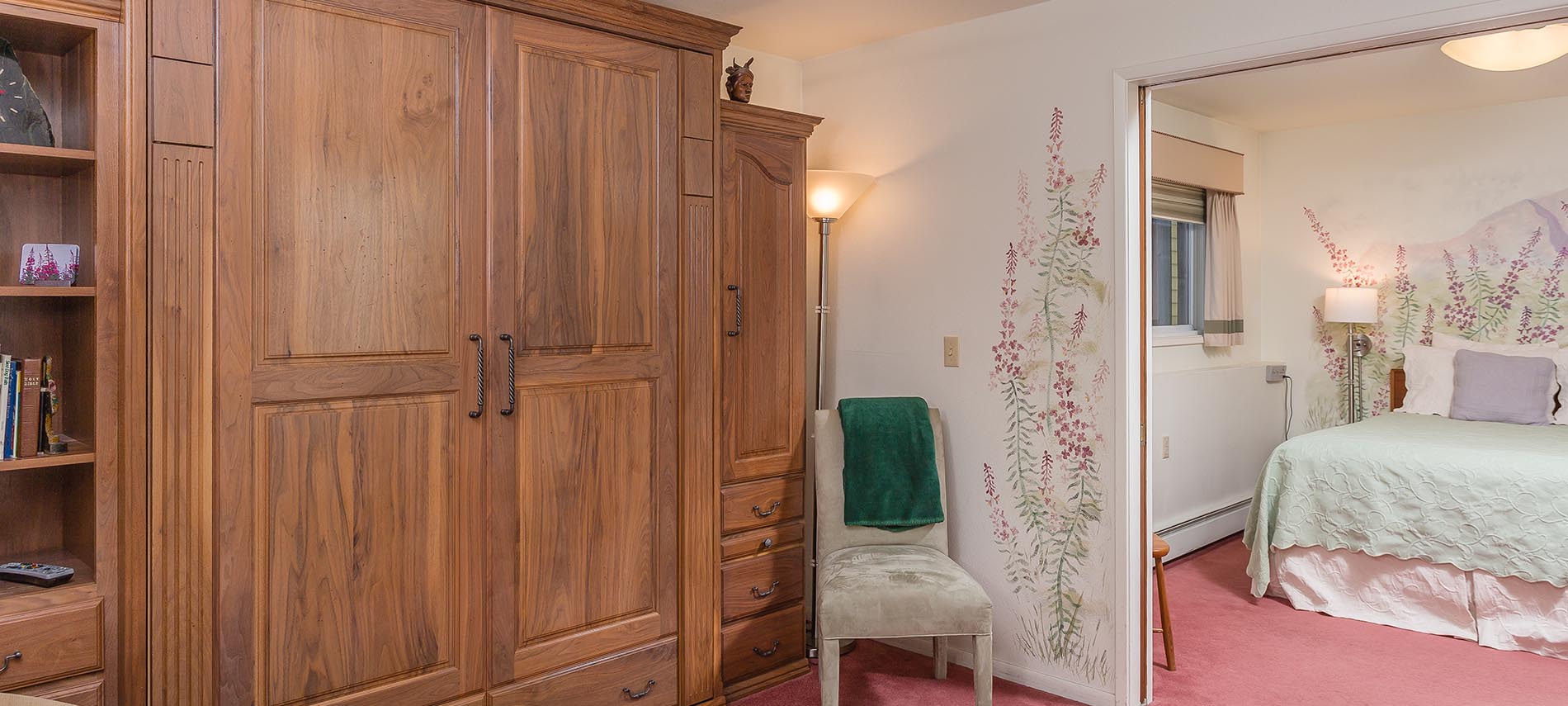 Queen bed with green spread; second room with two chairs and wood cabinetry; soft salmon-colored carpet