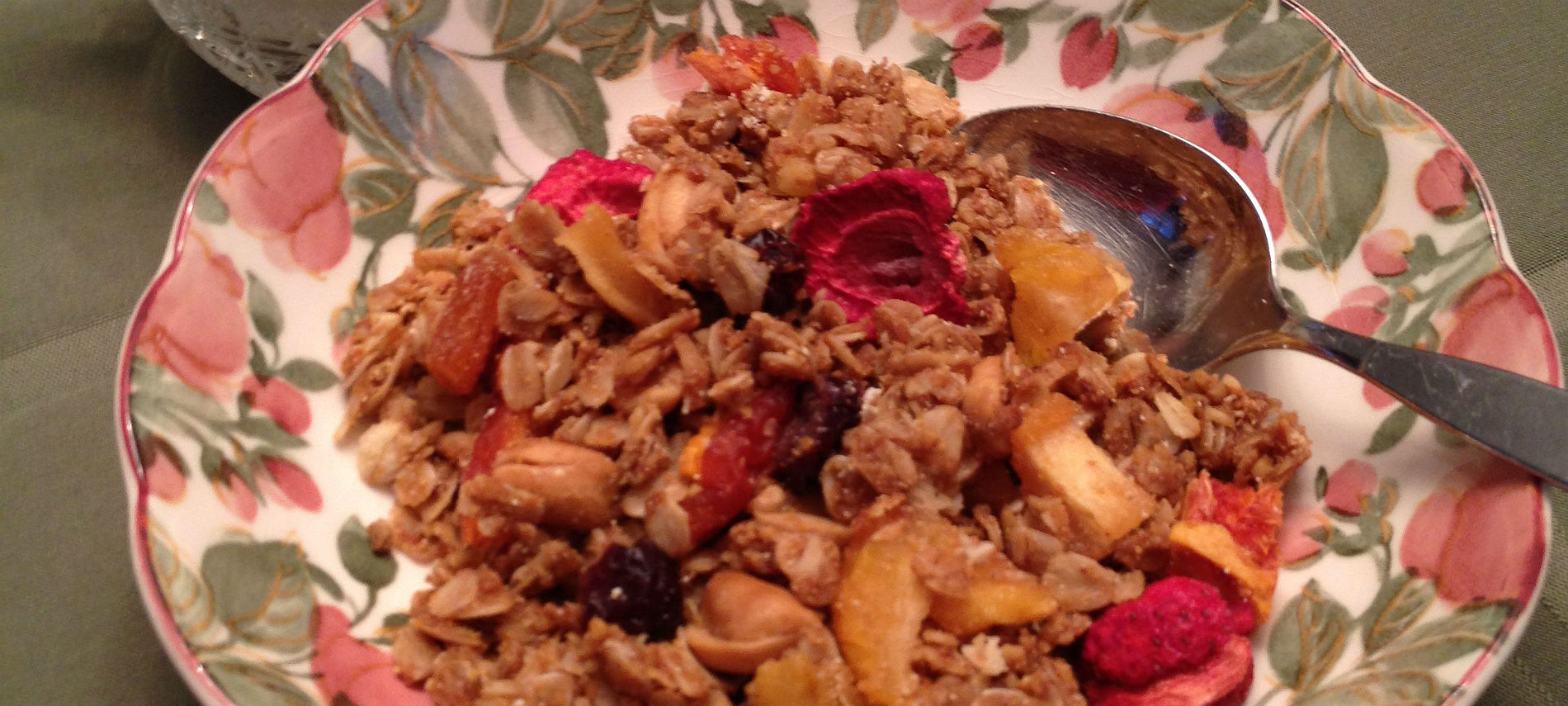 Flowered round bowl with silver spoon containing granola and dried strawberries.