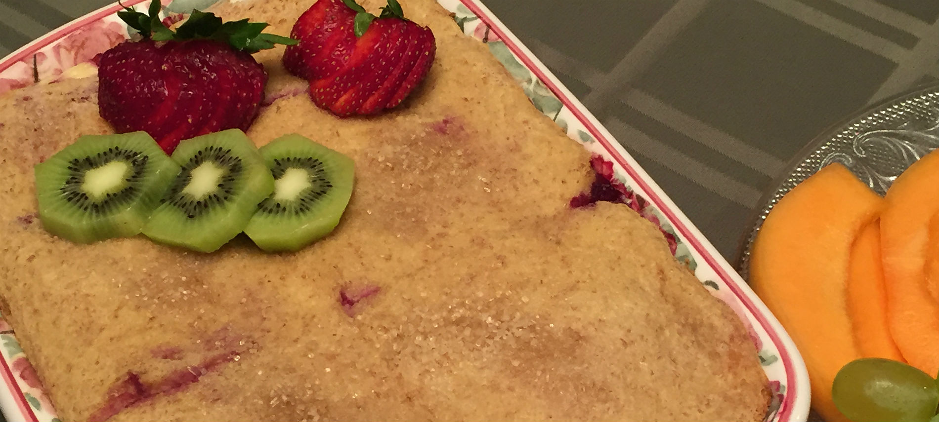 Rectangular dish with pastry, fresh kiwi and strawberries with stems, Cantaloupe and green grapes on glass dish.