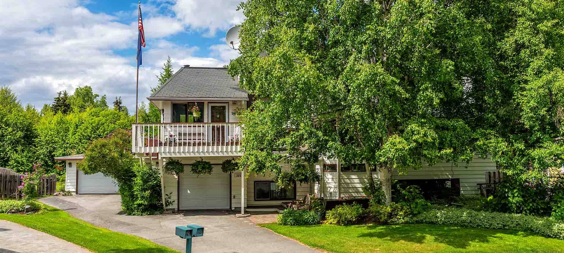 White 2-story home with 1 car garage surrounded by trees, detached 1 car garage, with flagpole with American flag flying, detached 2 car garage.