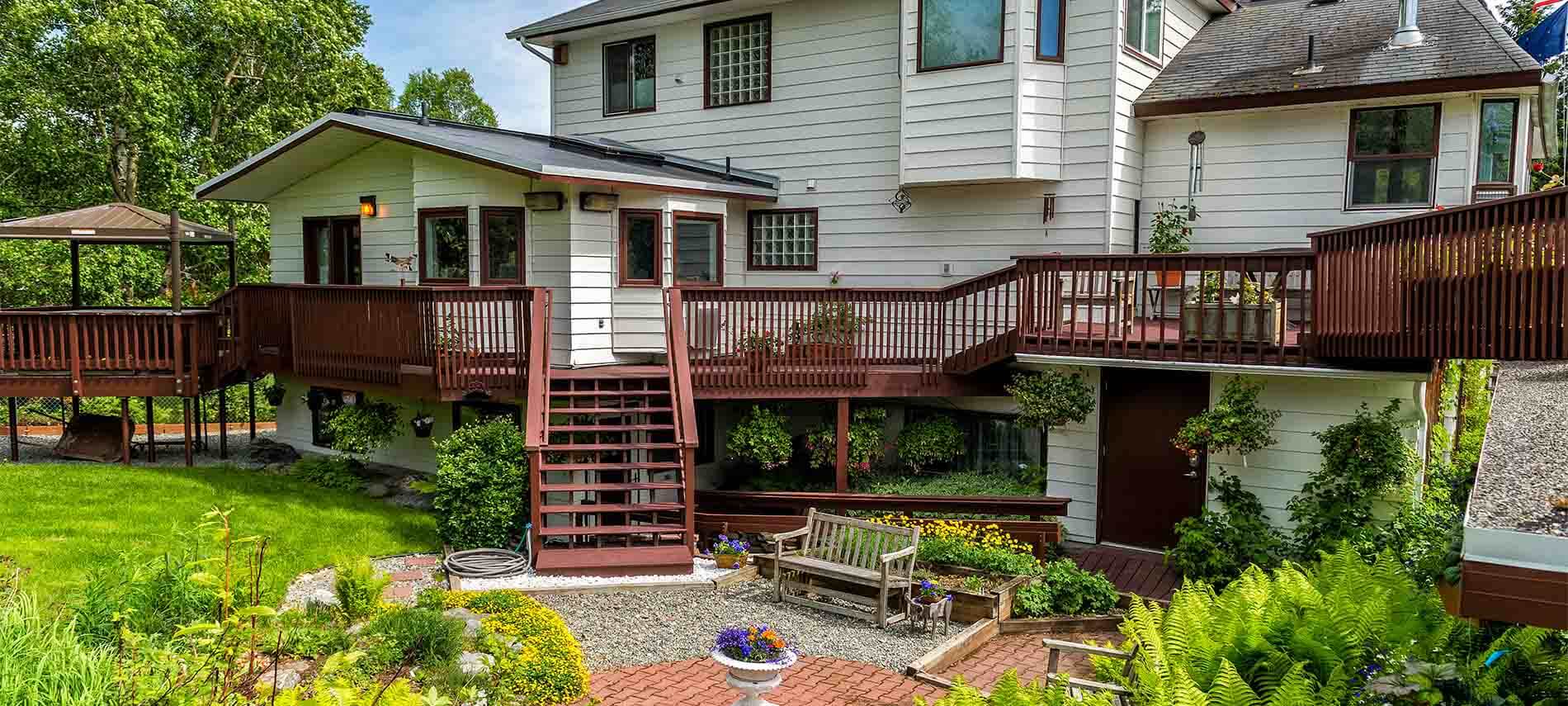 Back view of home with wrap around wooden deck, stairs to desck from lower level.