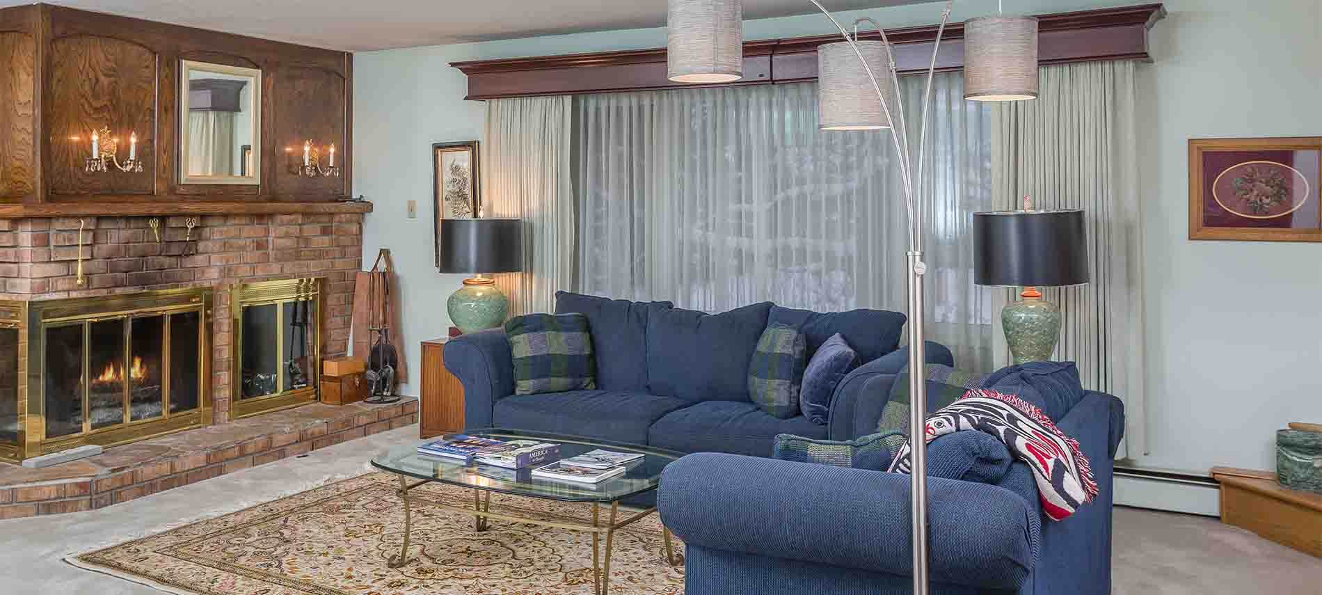 Sitting area with blue furniture, fireplace with mantel, standing lamp, picture window.